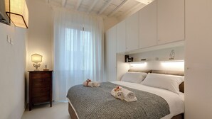 A hotel room with a bed, a nightstand, a lamp, and a window with curtains. - Mamo Florence - Brancacci Apartment (Florence)