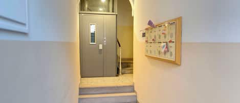 Un corridoio con una porta che dà su una scala, una bacheca con dei fogli e una lampada a soffitto.