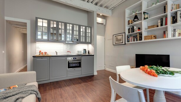 A modern kitchen with grey cabinets, a white countertop, and a dining area with a white table and chairs. - Mamo Florence - Cloe Apartment (Florence)