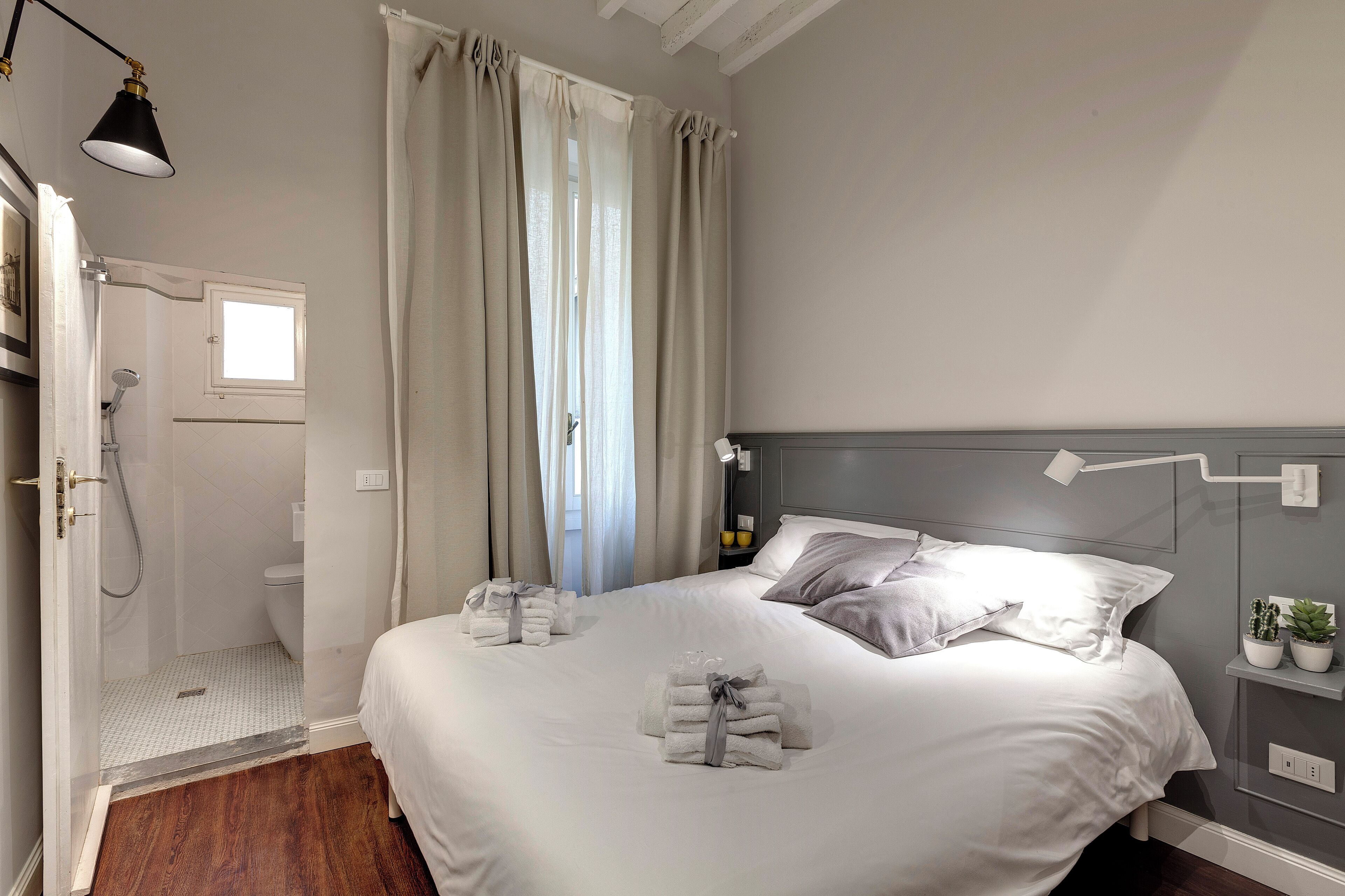 Une chambre d’hôtel avec un grand lit, une table de chevet avec une lampe, un espace douche et une fenêtre avec des rideaux.