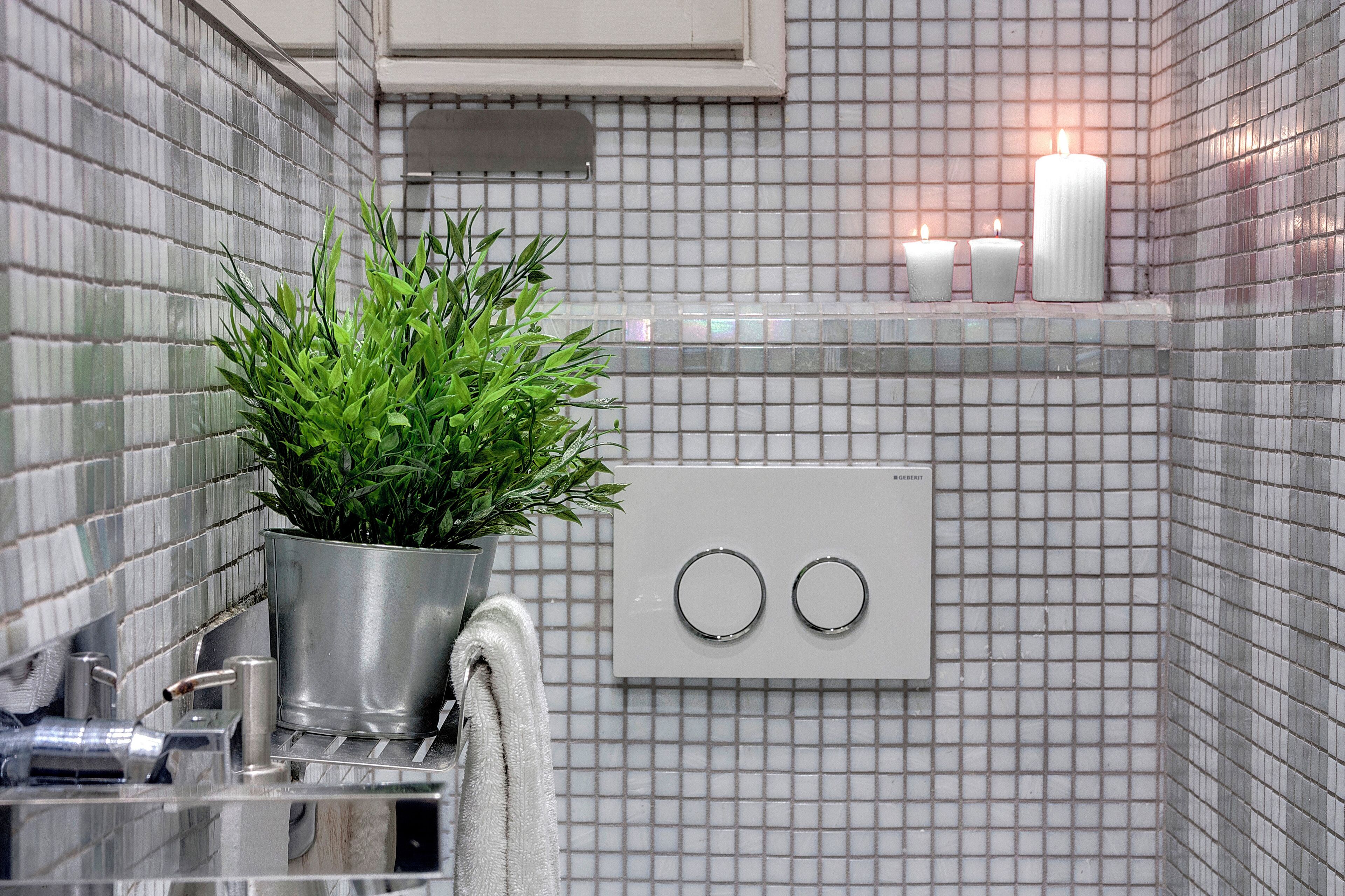 Ein Badezimmer mit gefliestem Rückspritzschutz, einer Topfpflanze, einem Handtuch und einem Lichtschalter.