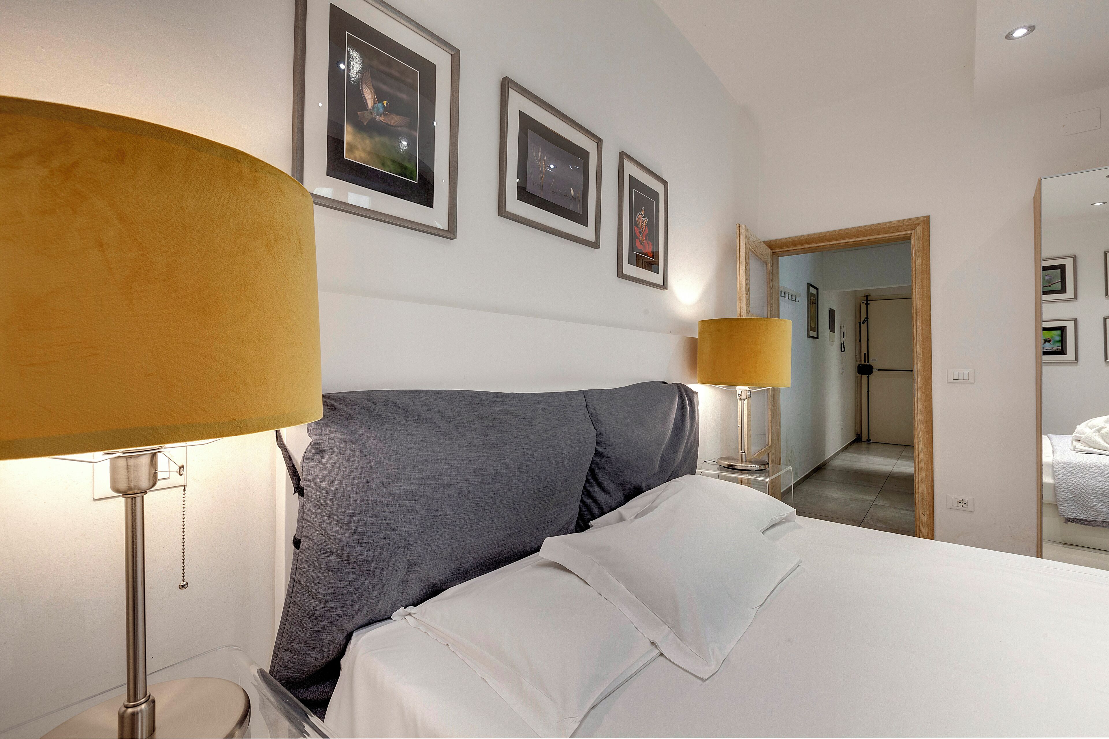 A hotel room with a bed, two bedside lamps, and three framed pictures on the wall.
