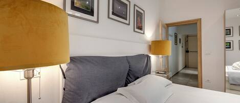 A hotel room with a bed, two bedside lamps, and three framed pictures on the wall.