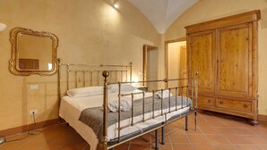 A bedroom with a metal bed frame, a wooden wardrobe, and a mirror on the wall. - Mamo Florence - Dafne Apartment (Florence)