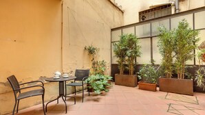 A courtyard with a table and chairs, potted plants, and a window with a view. - Mamo Florence - Dafne Apartment (Florence)