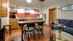 A kitchen with wooden cabinets, a dining table with chairs, a microwave, and a refrigerator. - Mamo Florence - Dafne Apartment (Florence)