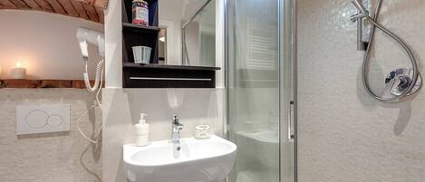 A bathroom with a glass shower enclosure, a white sink, and a towel rack.