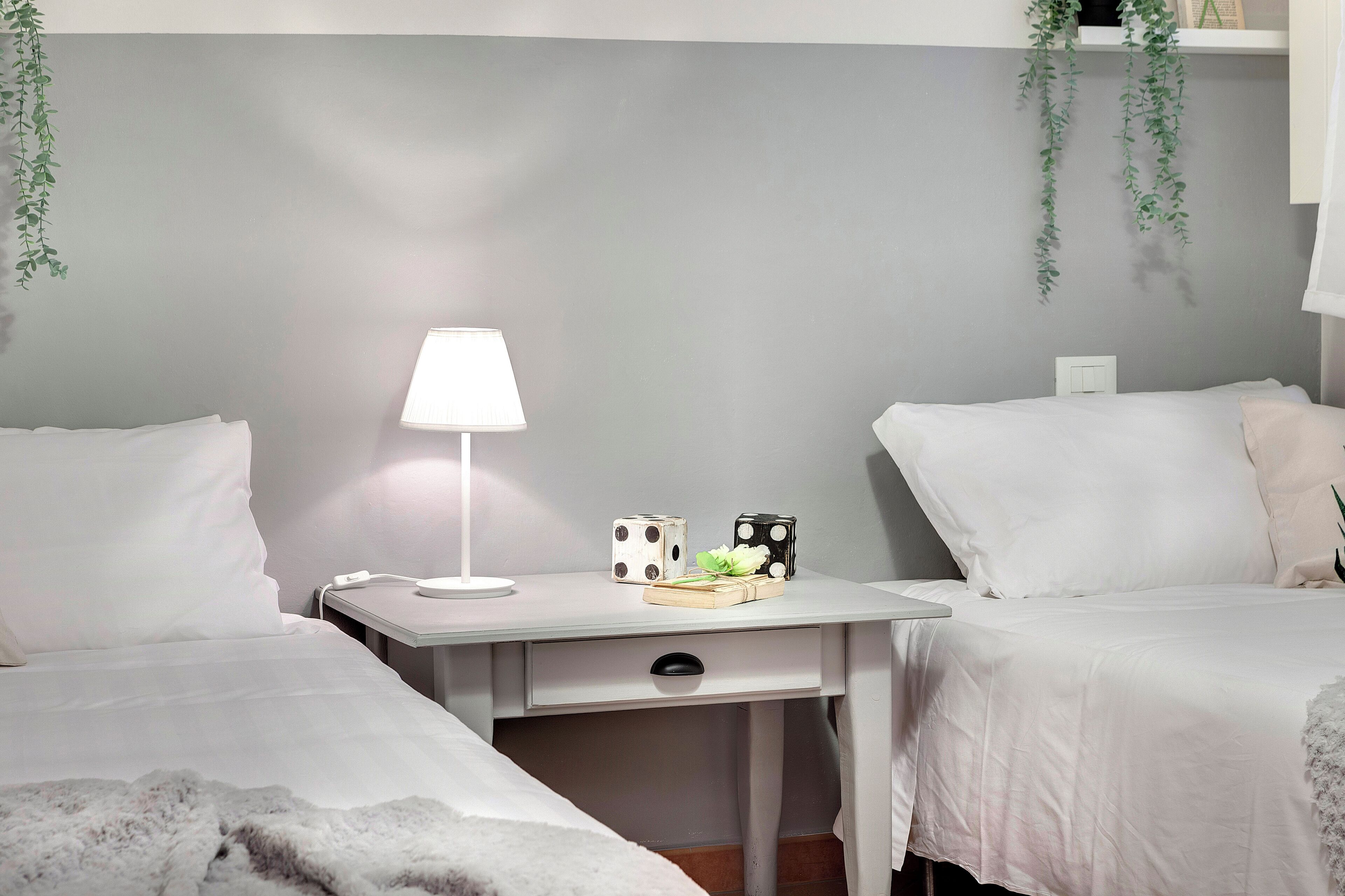 A hotel room with two beds, a bedside table with a lamp, and a small desk with a phone and dice.