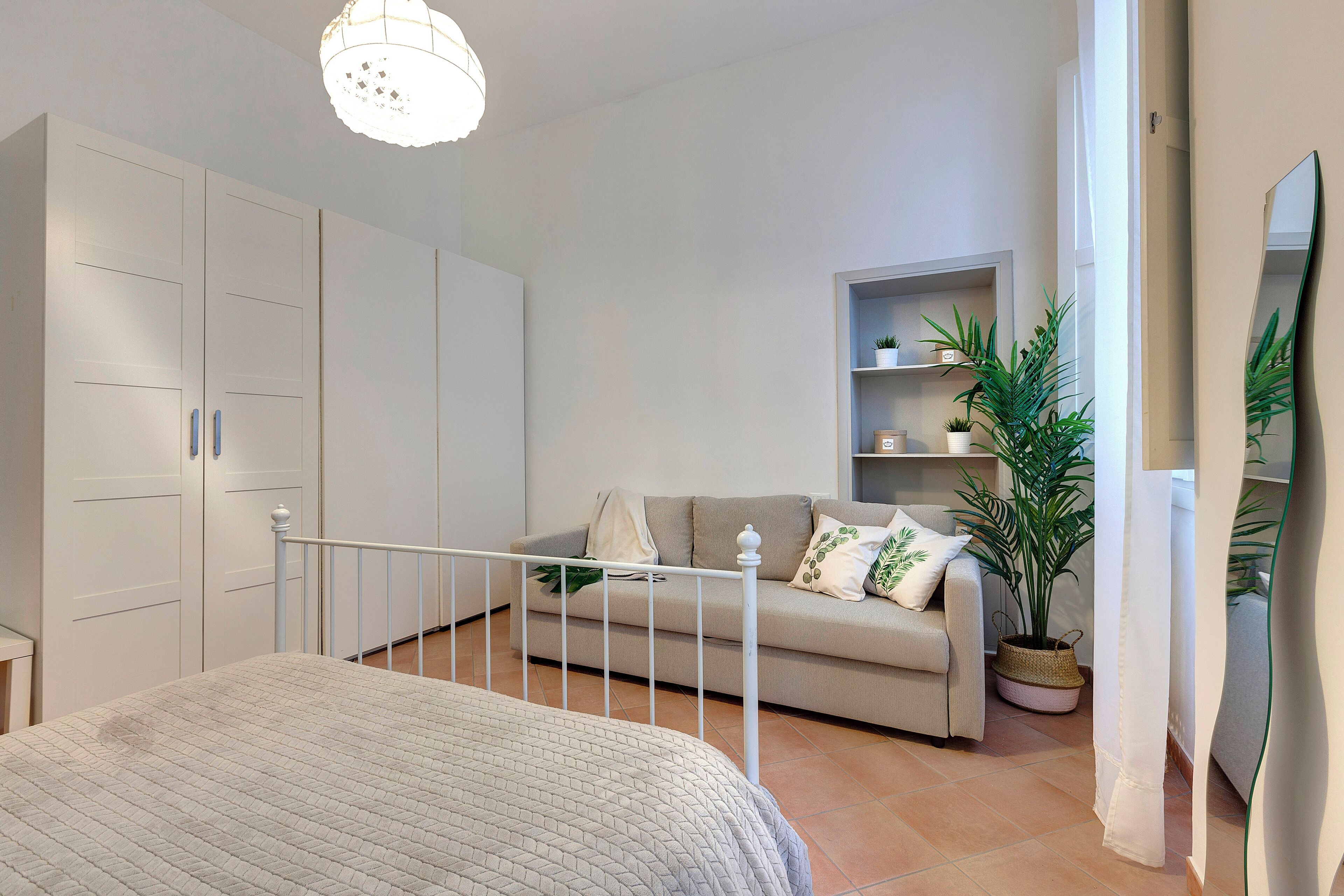 A bedroom with a bed, wardrobe, sofa, and potted plants.