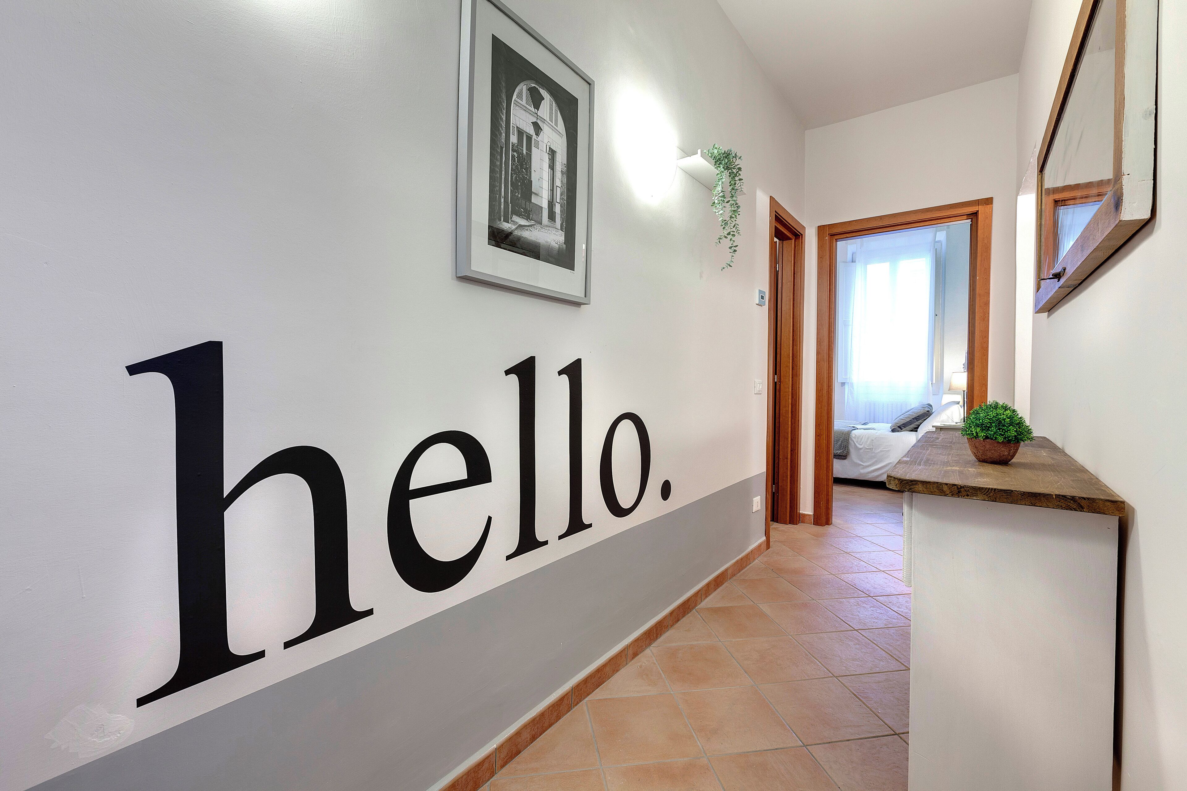 A hallway with a 'hello.' sign, a framed picture, and a potted plant.