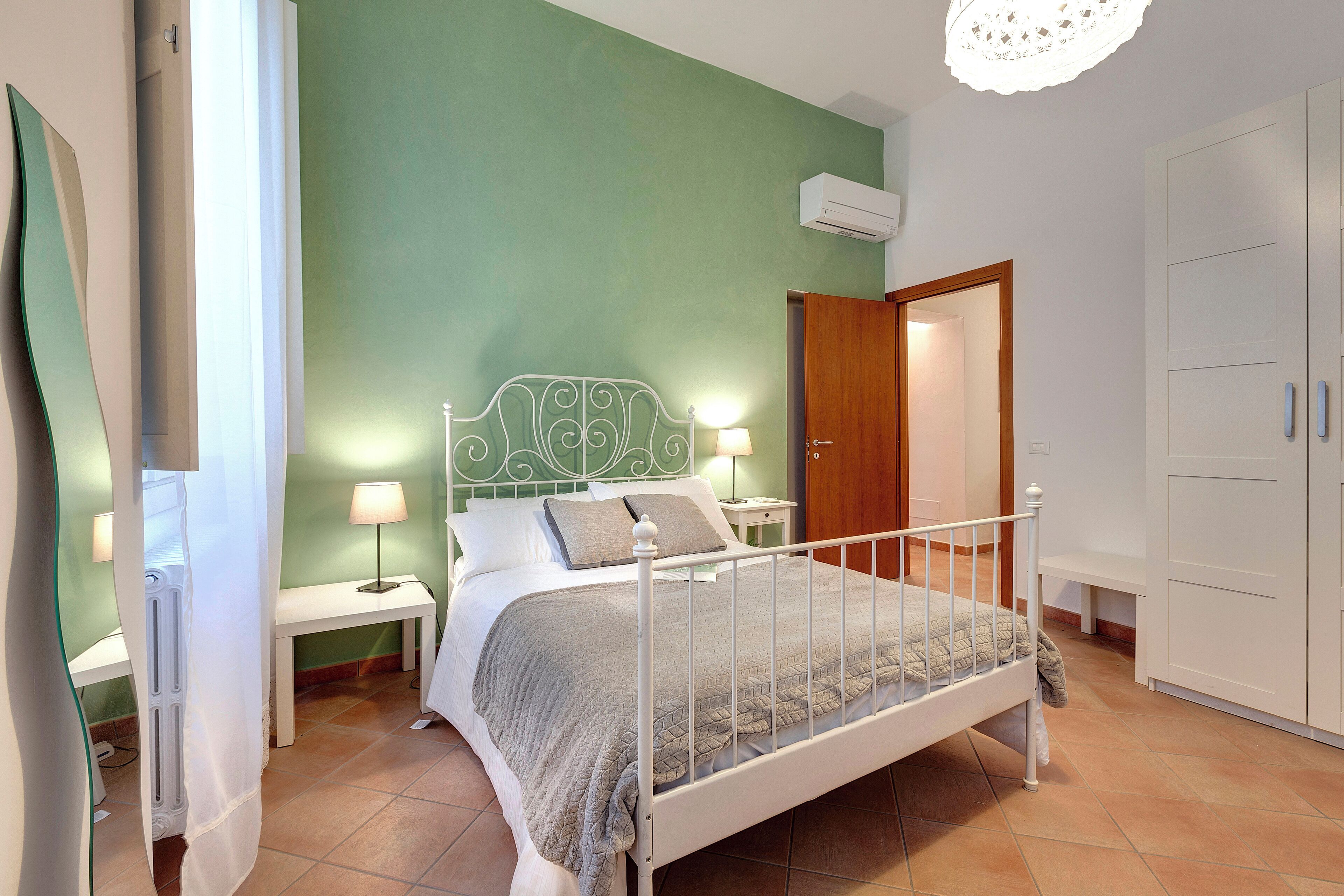 A bedroom with a bed, bedside tables, a nightstand, a wardrobe, and a mirror.