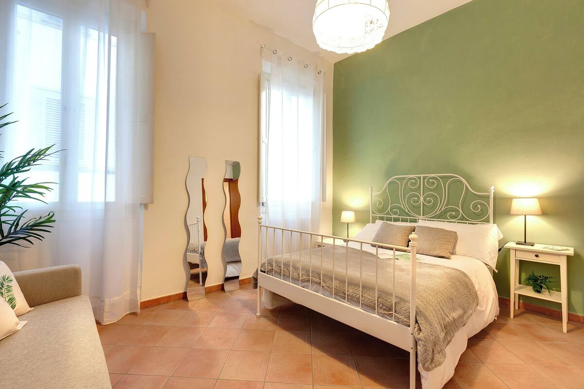 Ein Schlafzimmer mit einem Bett, Nachttischen, einem Sessel und einer Pflanze.