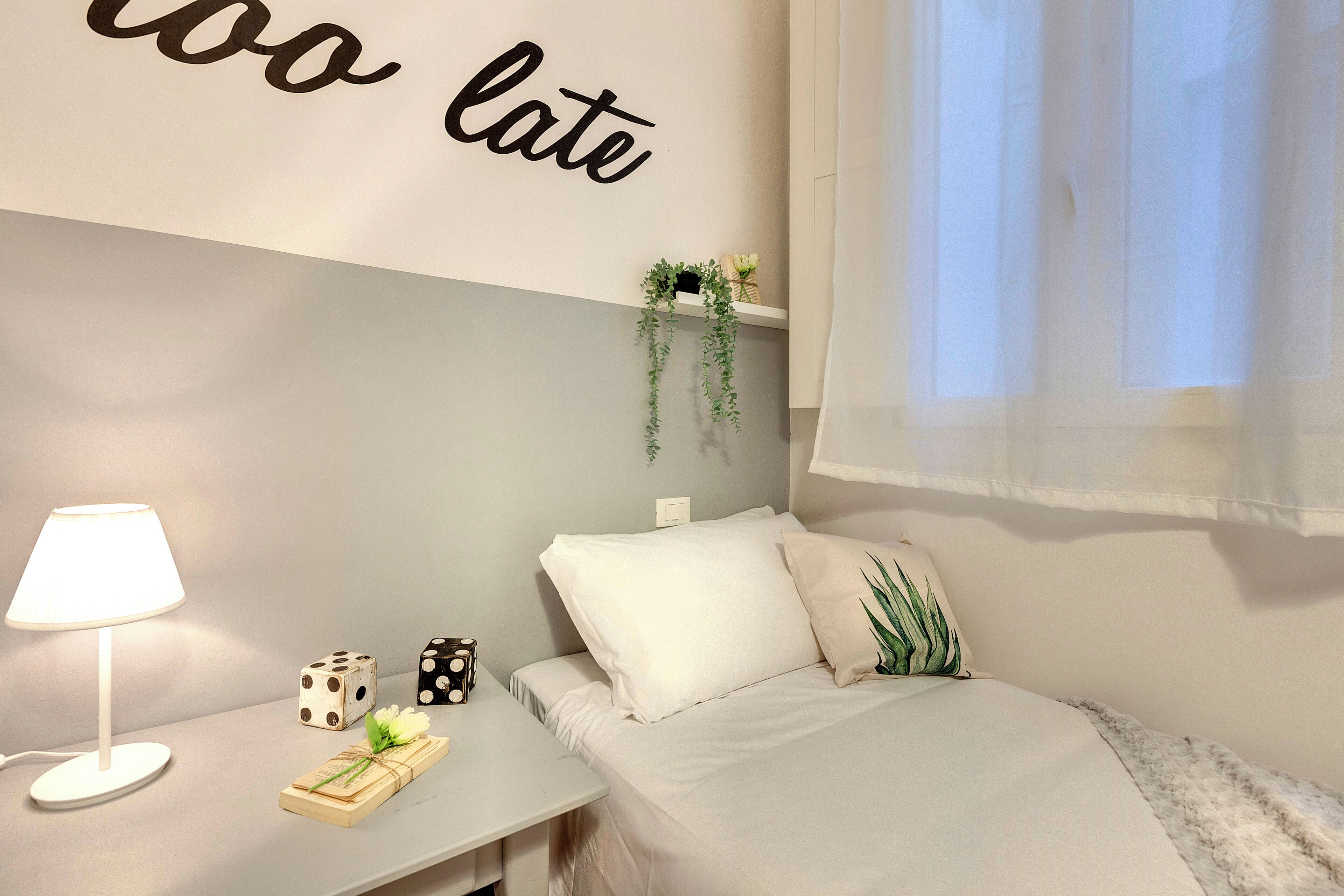 A neatly arranged bedroom with a bed, a bedside table with a lamp, dice, and a small plant.