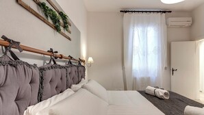 Un lit bien fait, avec du linge de lit blanc, une tête de lit à motifs capitonnés et une tringle à rideaux en bois ornée d’un nœud.