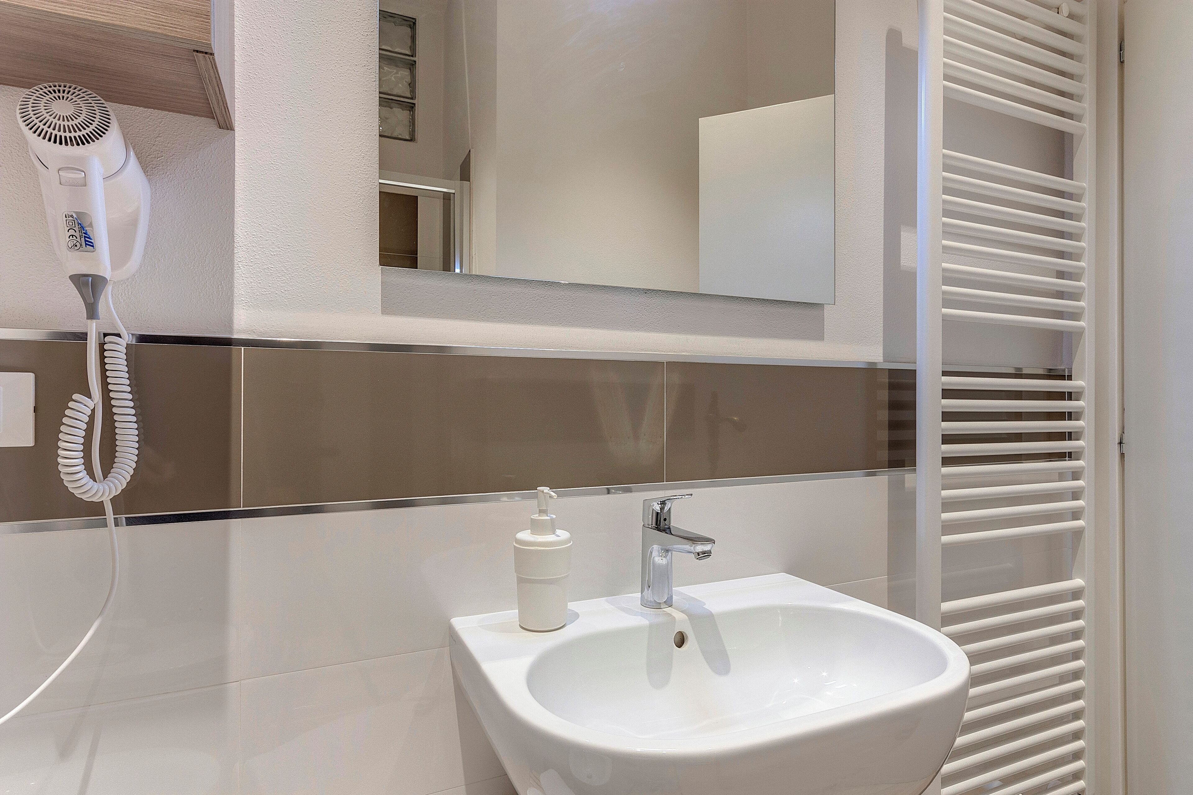 Een moderne badkamer met een wit wastafel, een haardroger en een spiegel.