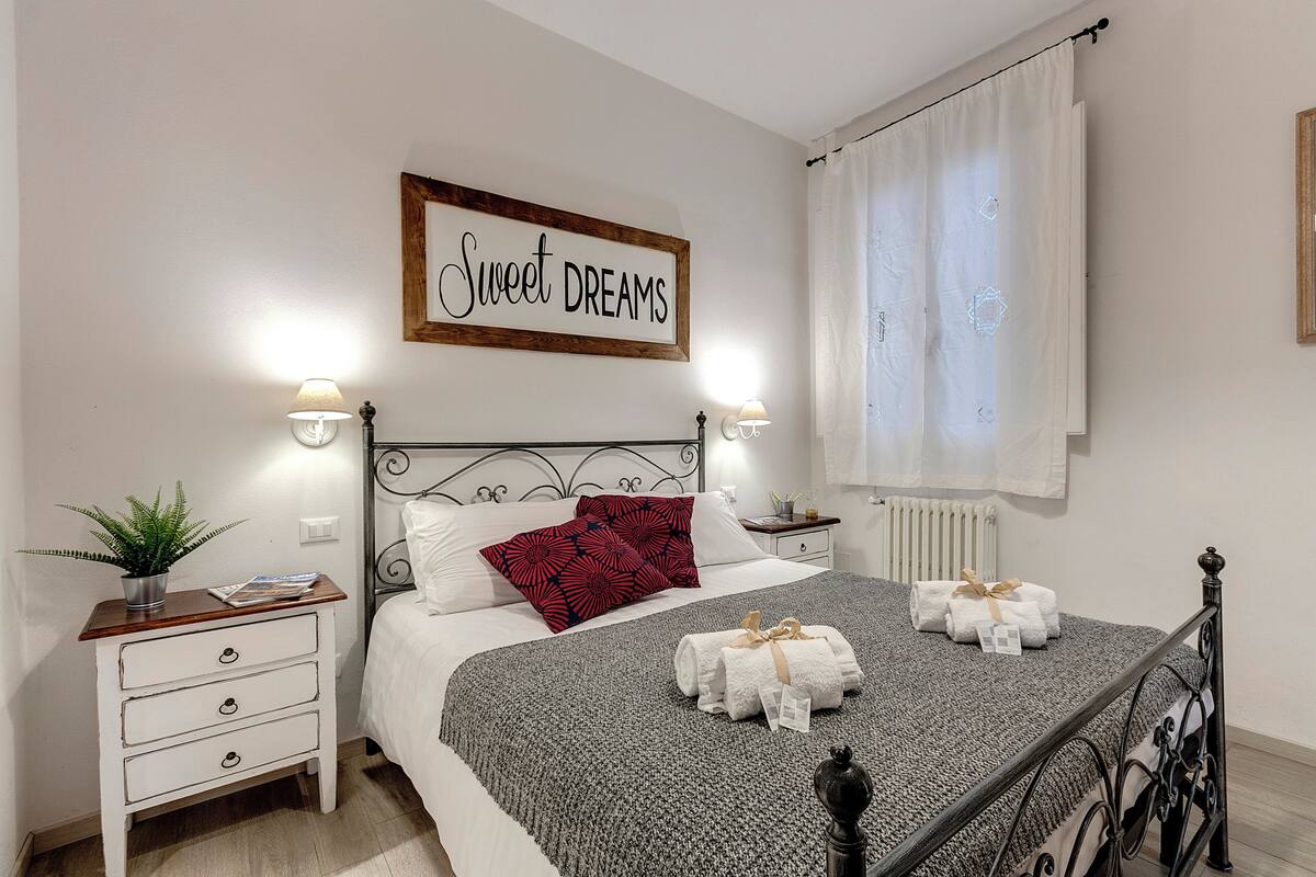 Ein ordentlich eingerichtetes Schlafzimmer mit einem Bett, Nachttischen, einem an der Wand befestigten Schild und einem Fenster mit Vorhängen.