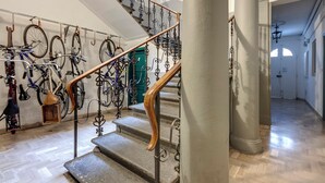 Un escalier orné de rampes en métal ouvragé et doté d’une main courante en bois, menant à une pièce où se trouvent des vélos et une porte verte.