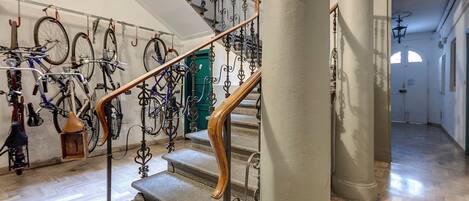 A staircase with ornate metal railings and a wooden handrail, leading to a room with bicycles and a green door.