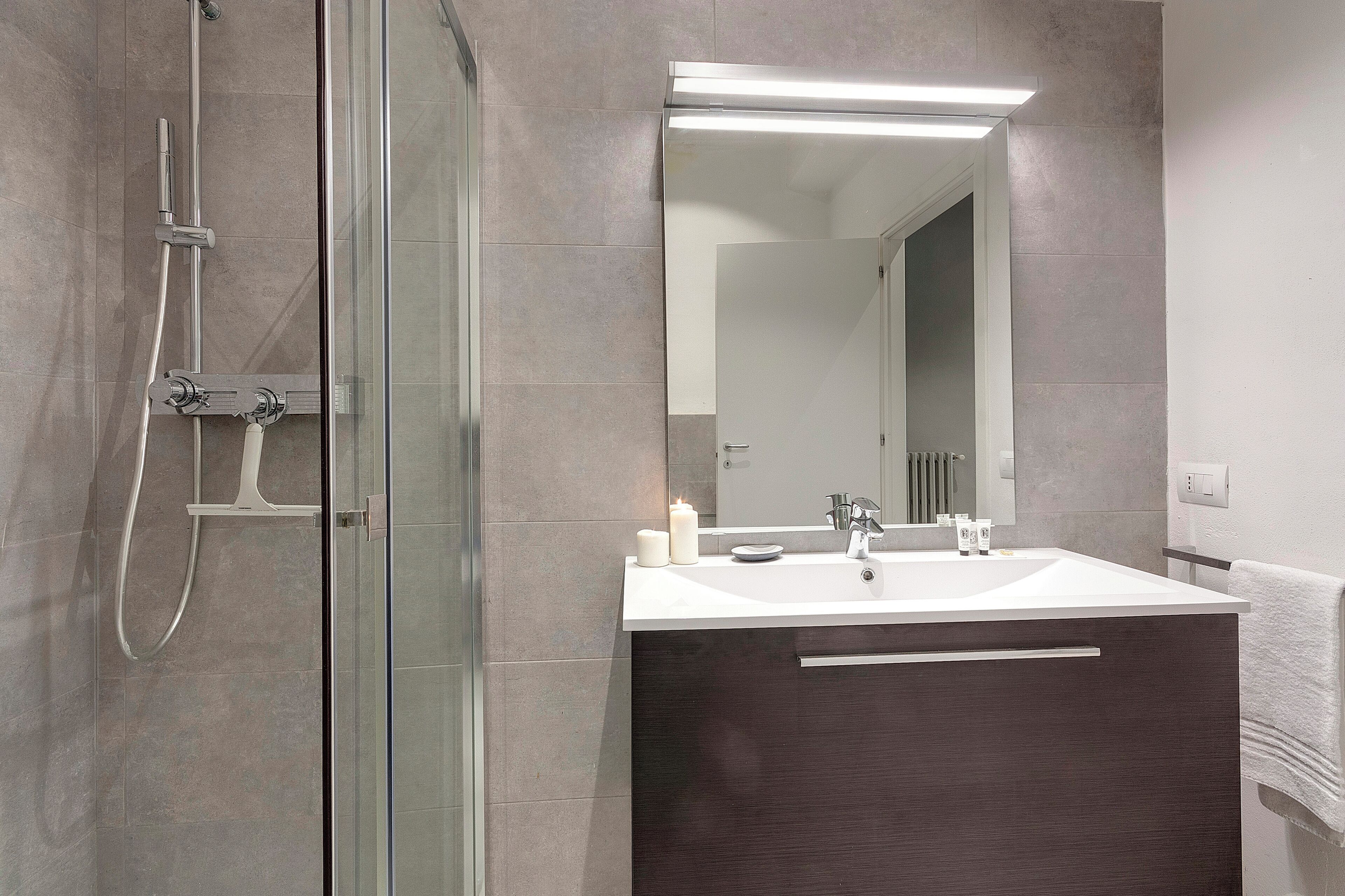 A modern bathroom with a glass shower enclosure, a white sink with a dark vanity, and a mirror above the sink.