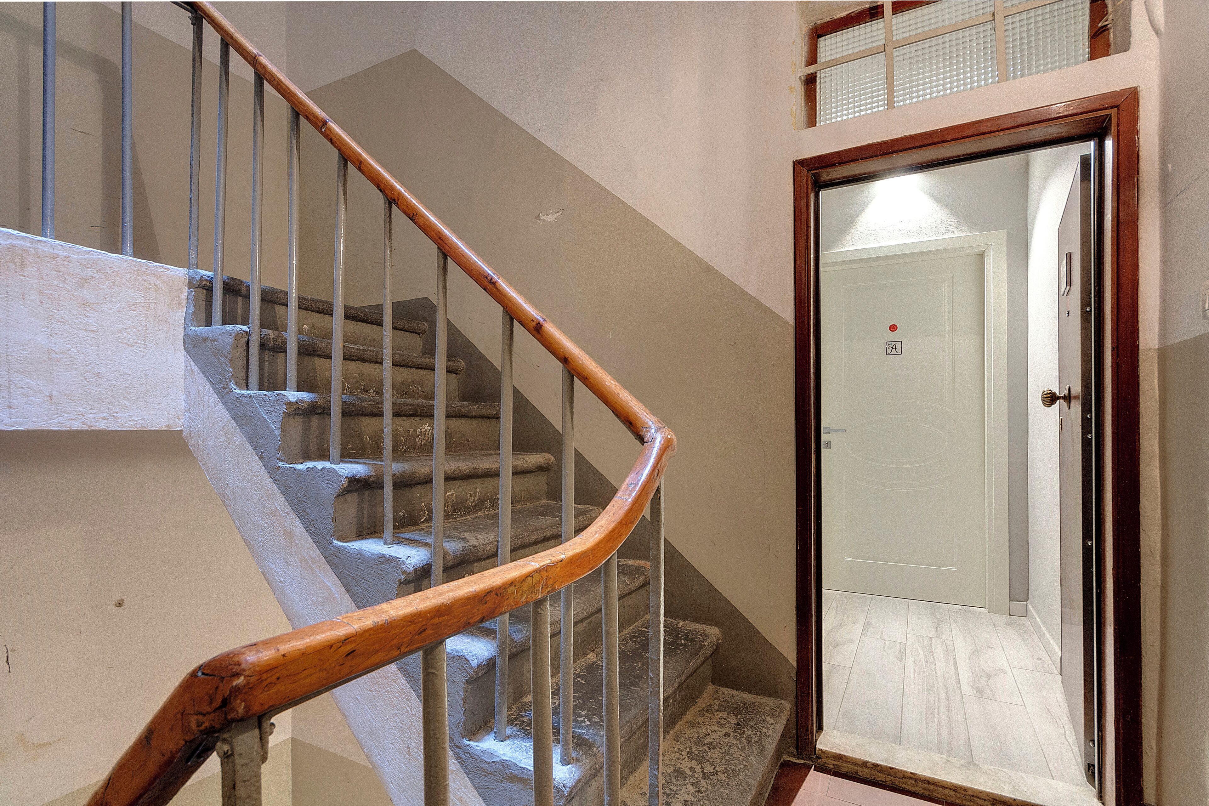 Un escalier avec des rampes en bois et des balustrades en métal, menant à une porte sur laquelle est fixée une petite plaque.
