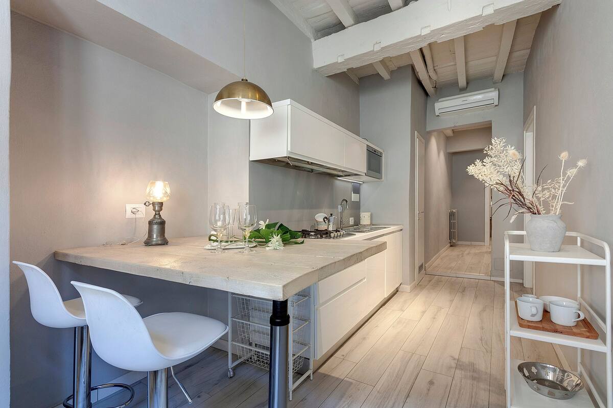Une cuisine moderne avec des meubles blancs, un coin bar doté de tabourets et un luminaire suspendu.
