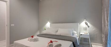 A neatly made bed with white linens and red ties, two bedside tables with lamps, and a ceiling fan.