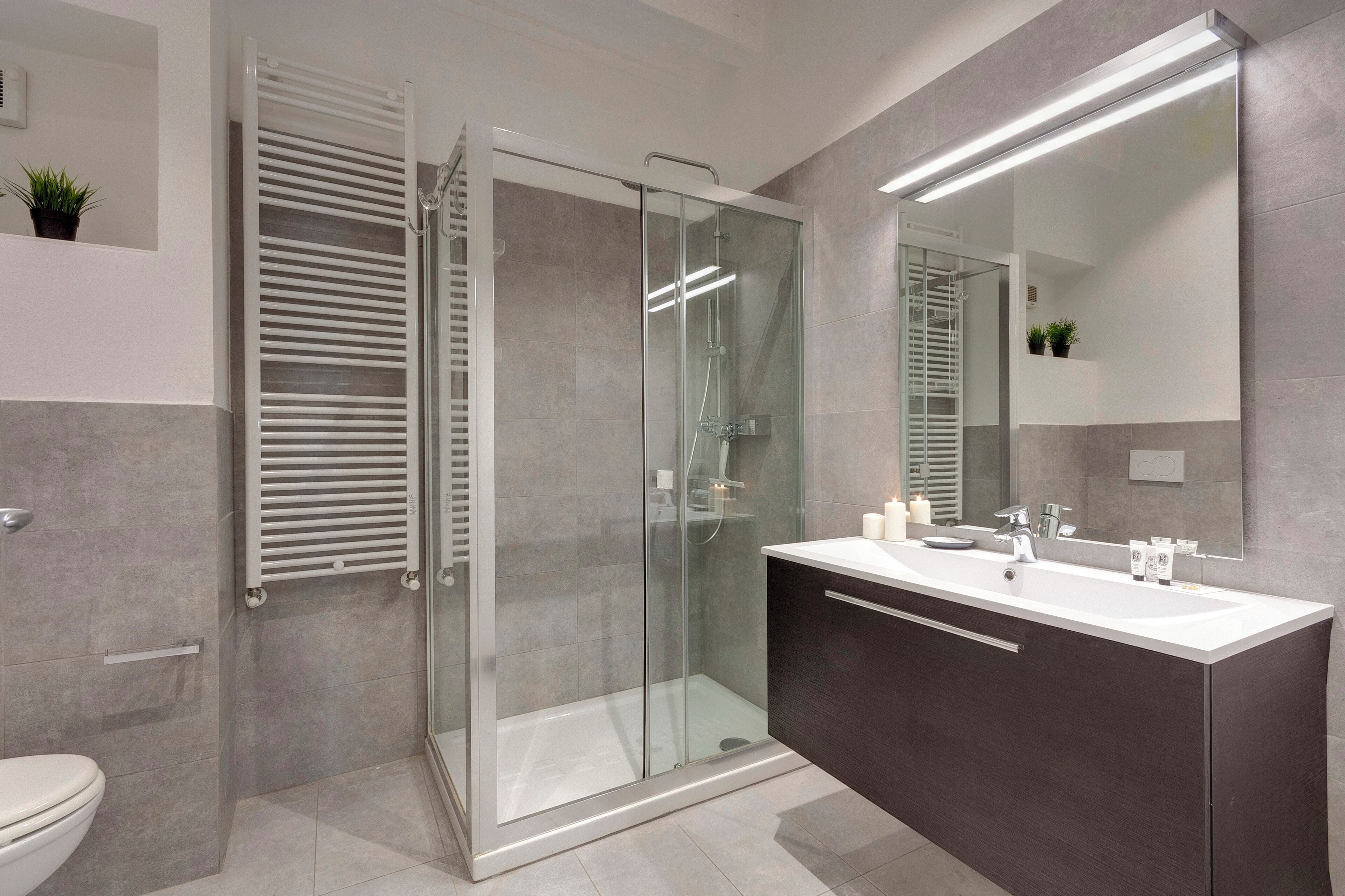 Een moderne badkamer met een douchecabine van glas, een wastafel met een grote spiegel en een toilet.
