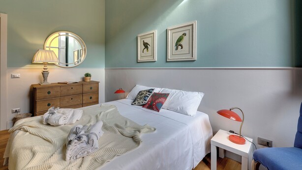 Un dormitorio con cama, mesita de noche, lámpara, cómoda y dos cuadros en la pared.