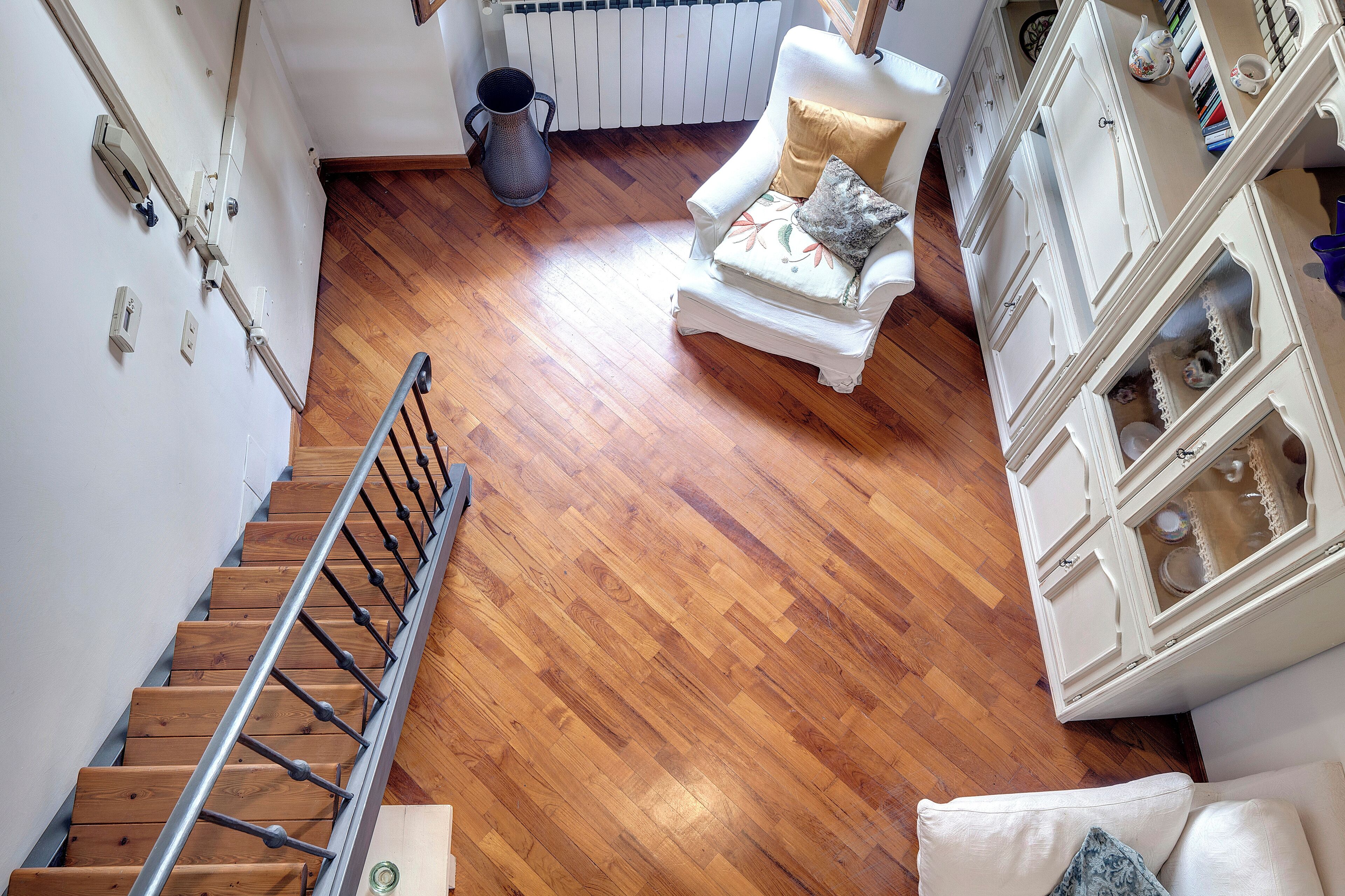 Eine Treppe führt zu einem Raum mit Holzboden, einem weißen Sessel mit Kissen und einem Schrank mit Glastüren.