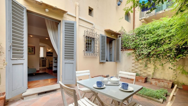 Un patio exterior con una mesa preparada para dos personas, rodeado de sillas blancas.