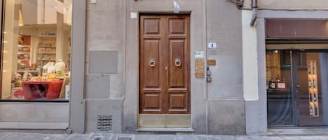 Un edificio con una porta in legno a due ante, una piccola finestra con inferriata in metallo e un cartello che indica un appartamento con una camera da letto.