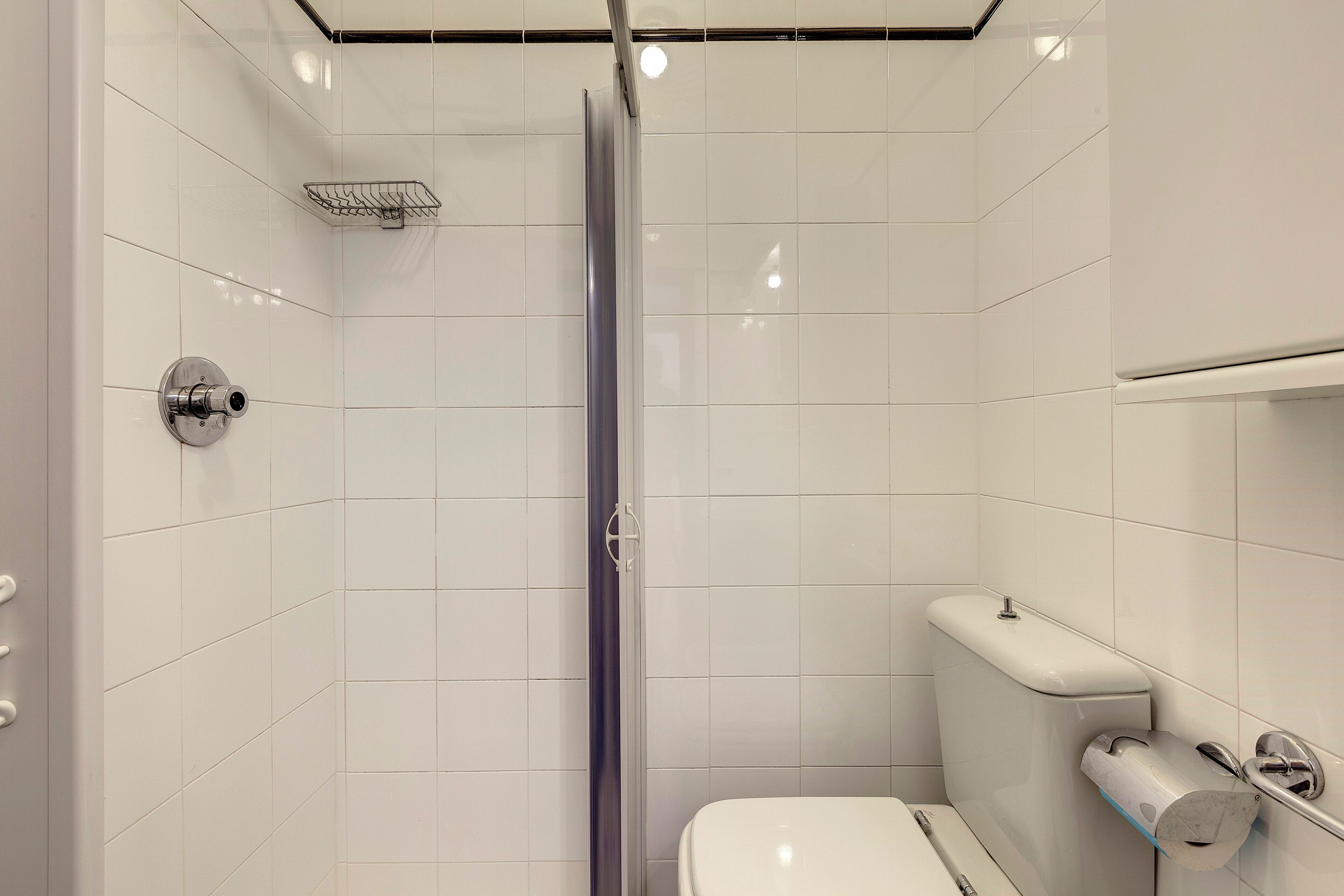 Um banheiro moderno com azulejos brancos, box de vidro, vaso sanitário e dispensador de toalhas de papel.