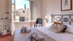 A hotel room with a bed, a chair, a desk, and a window with a view of buildings. - Mamo Florence - Guendalina Apartment (Florence)