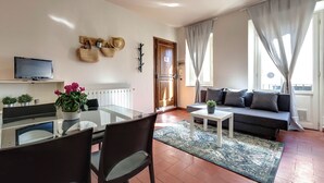 A modern living room with a glass dining table, black chairs, a grey sofa, and a TV mounted on the wall. - Mamo Florence - Guendalina Apartment (Florence)