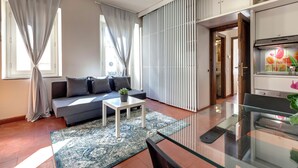 A modern living room with a sofa, a glass table, and a kitchen area with a stove. - Mamo Florence - Guendalina Apartment (Florence)