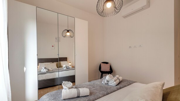 Een moderne slaapkamer met een grote spiegel, een bed met netjes opgevouwen handdoeken, een fauteuil en een bijzondere lamp.