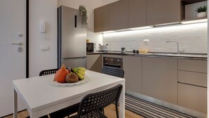 Een moderne keuken met een witte tafel, zwarte stoelen en een schaal met fruit.