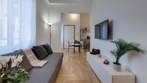 Een moderne woonkamer met een bank, een eethoek en een aan de muur bevestigde televisie.
