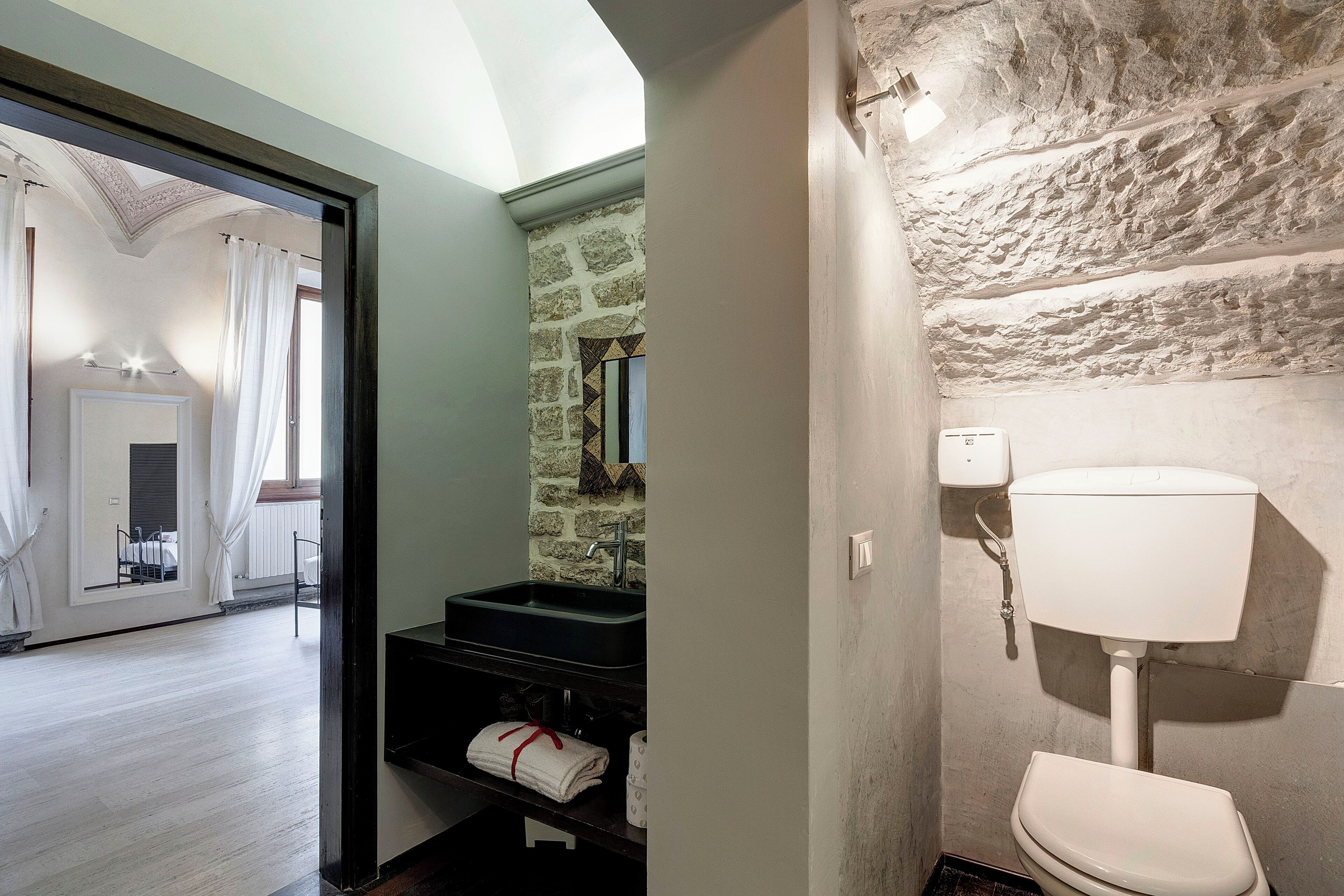 A bathroom with a stone wall, a white toilet, and a black sink.