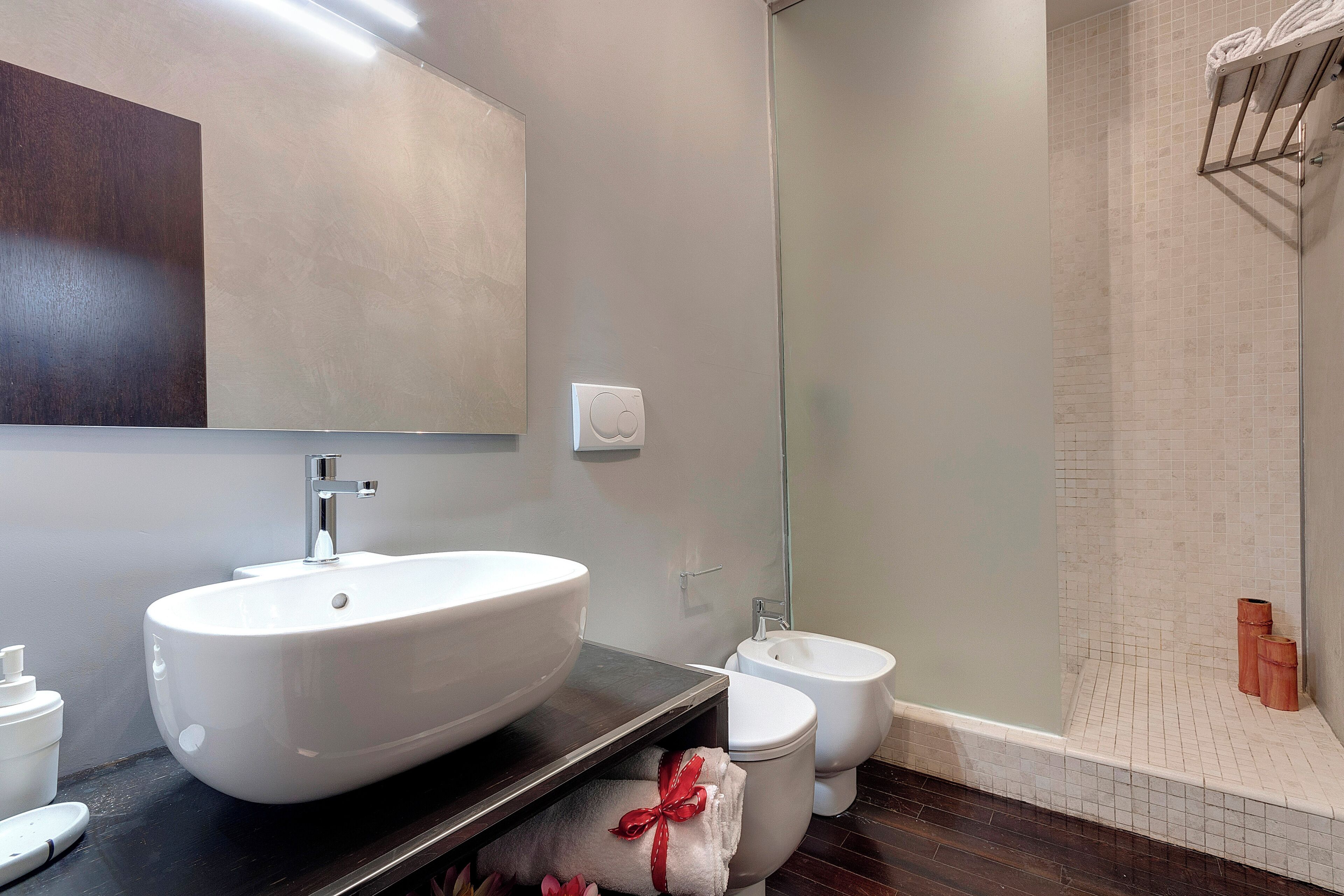 A modern bathroom with a large white sink, a bidet, and a glass shower enclosure.