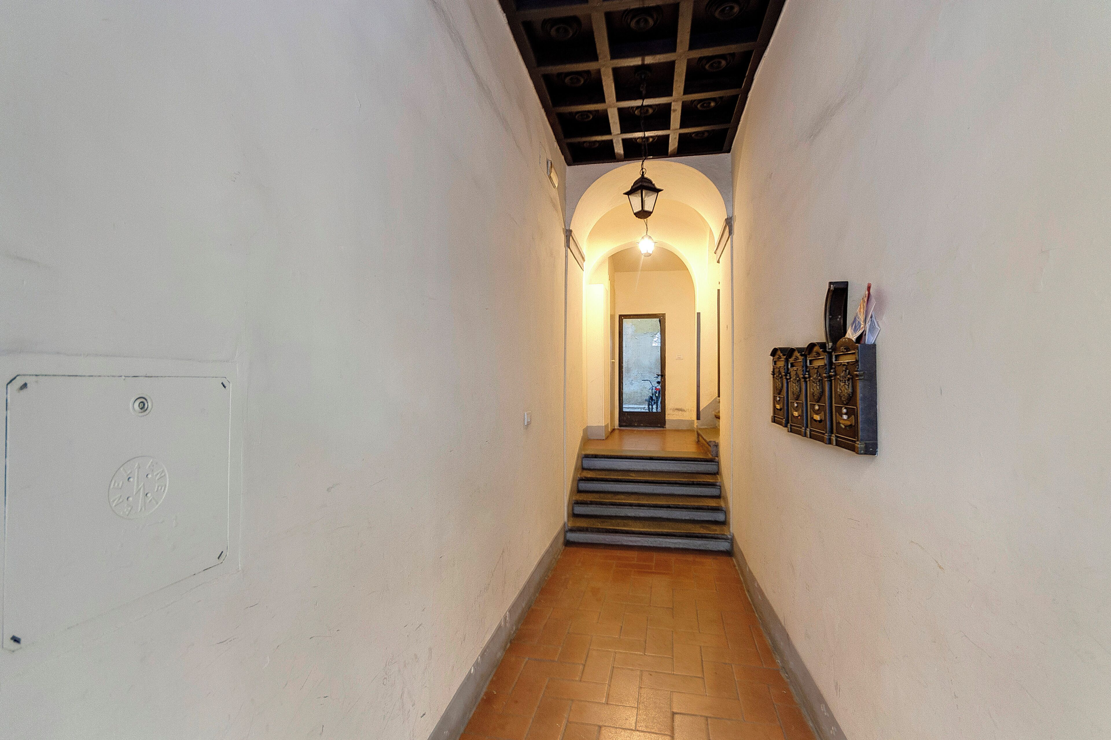 A narrow hallway with a tiled floor, a door at the end, and a light fixture above the door.