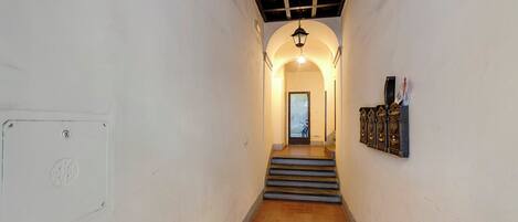 A narrow hallway with a tiled floor, a door at the end, and a light fixture above the door.