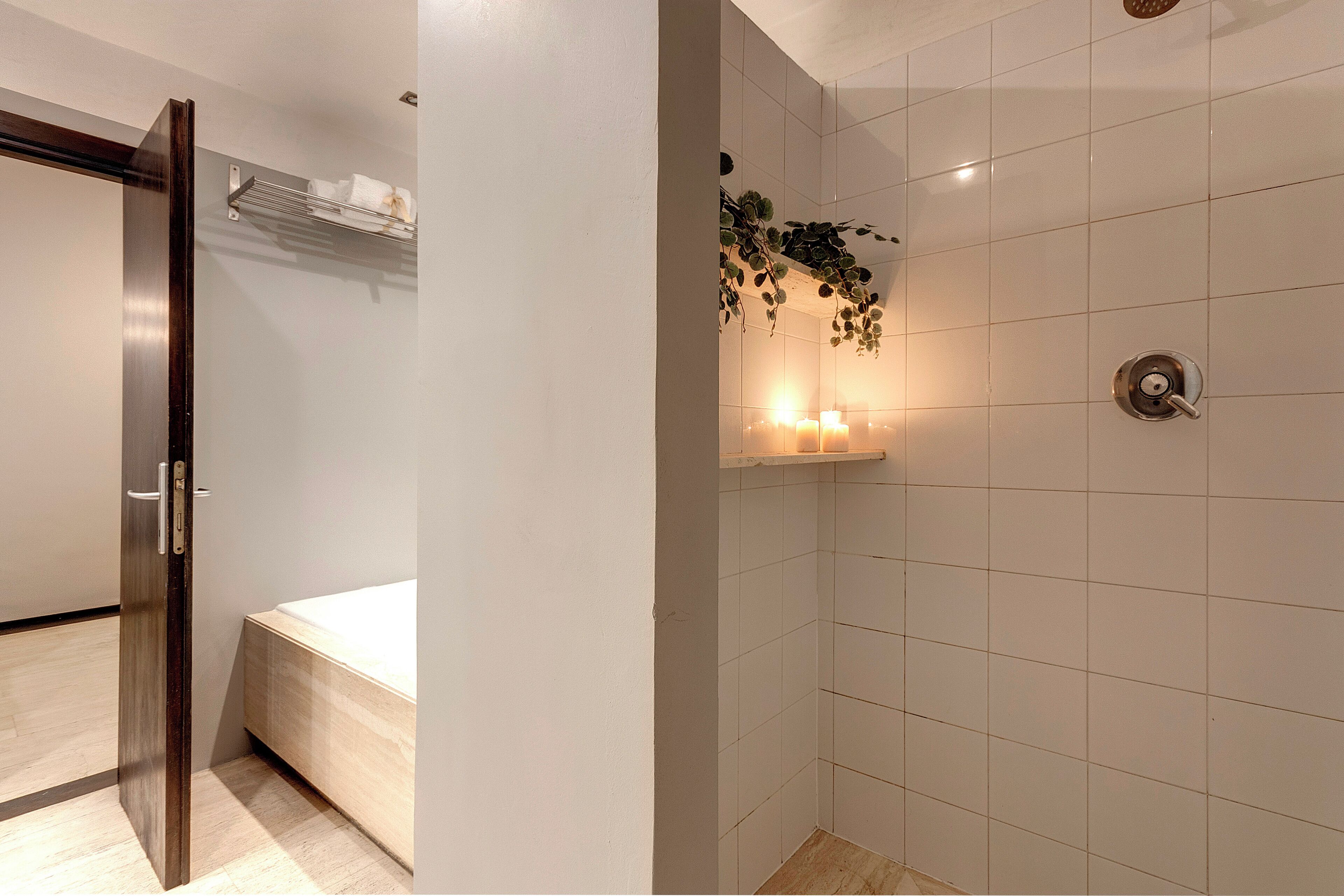 Ein Badezimmer mit weißen Fliesen, einer Duschkabine, einem Handtuchhalter und einem kleinen Regal mit Pflanzen.