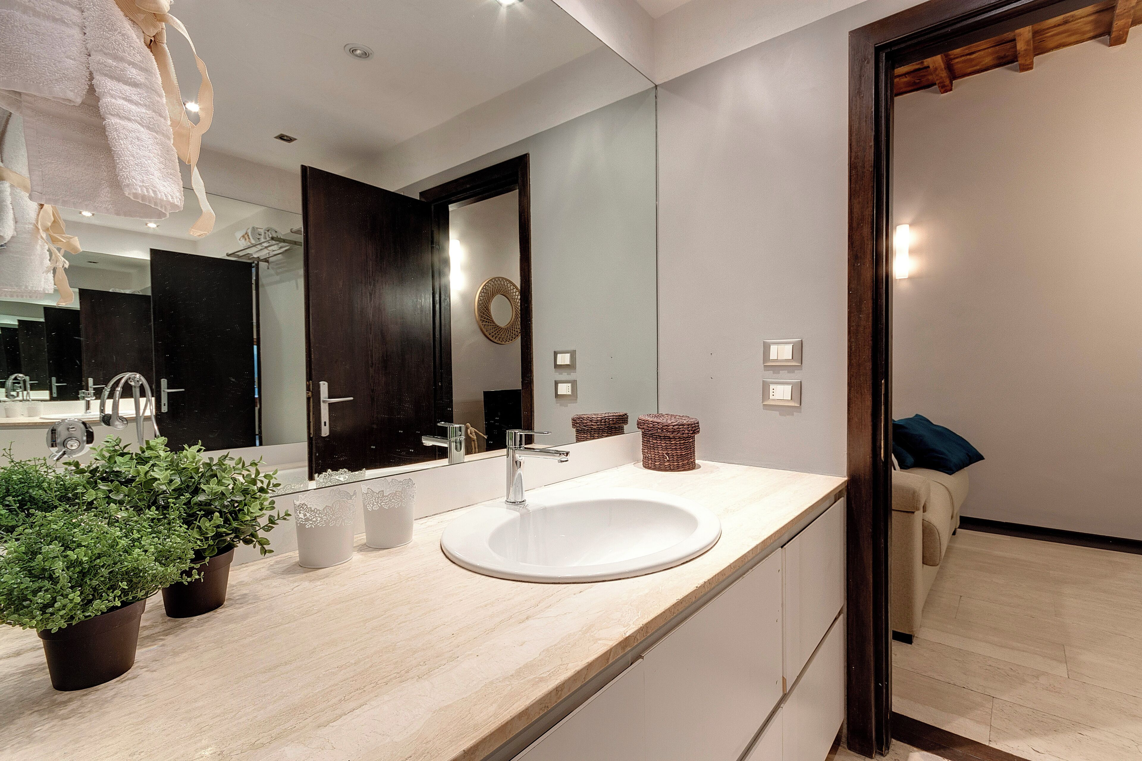 Une salle de bain moderne avec un grand miroir, un lavabo blanc et des plantes en pot.