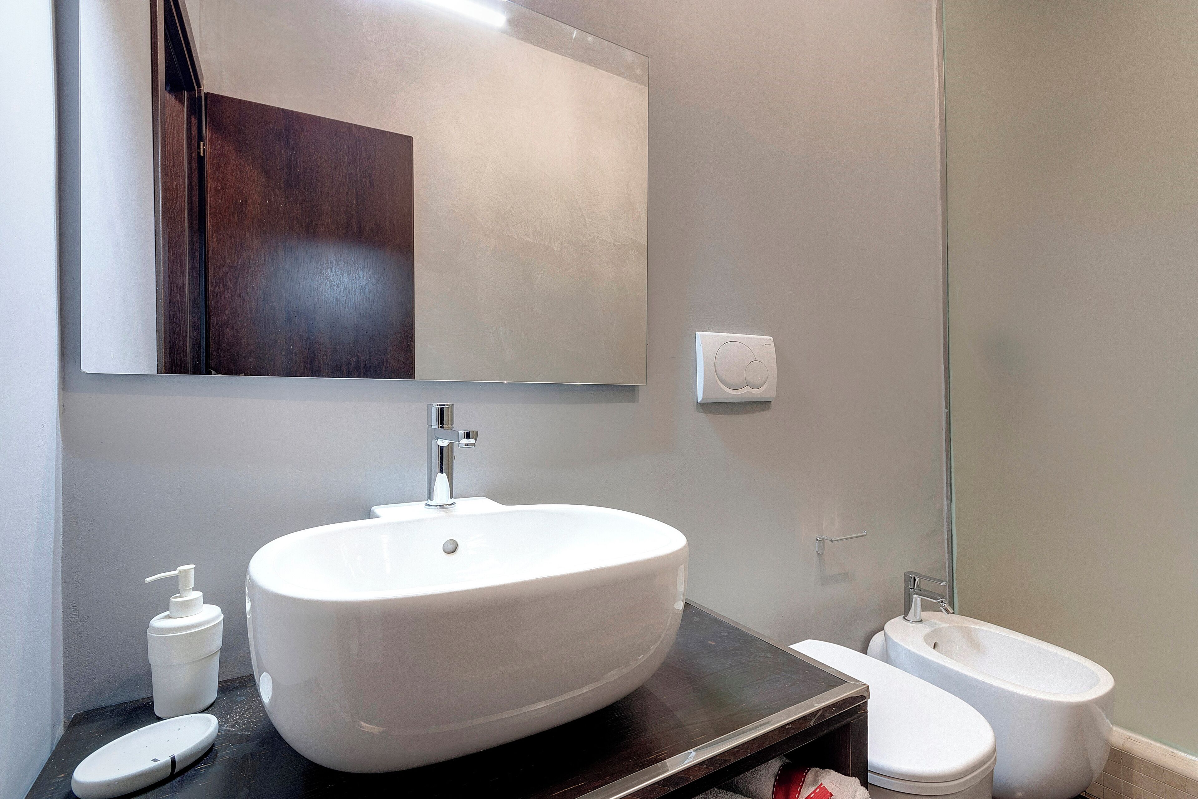 A bathroom with a large white sink, a mirror, a dark countertop, a toilet, and a bidet.