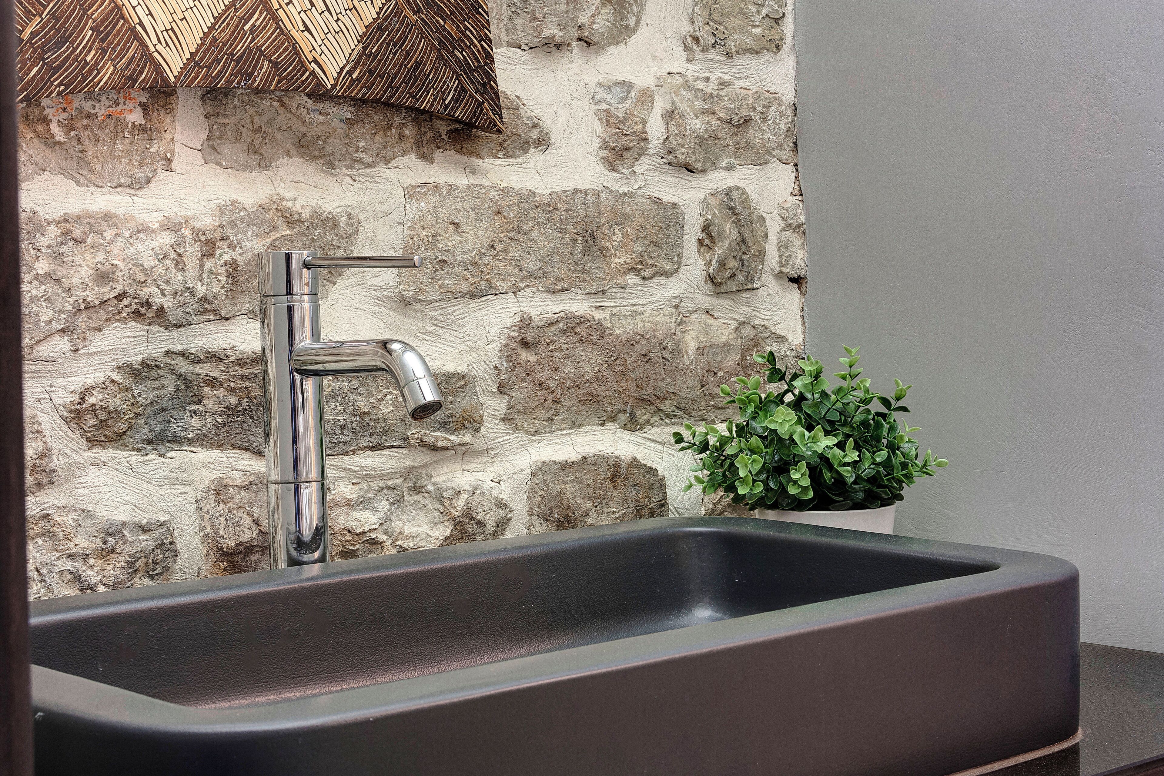 A modern kitchen with a stainless steel sink, a stone backsplash, and a small potted plant.