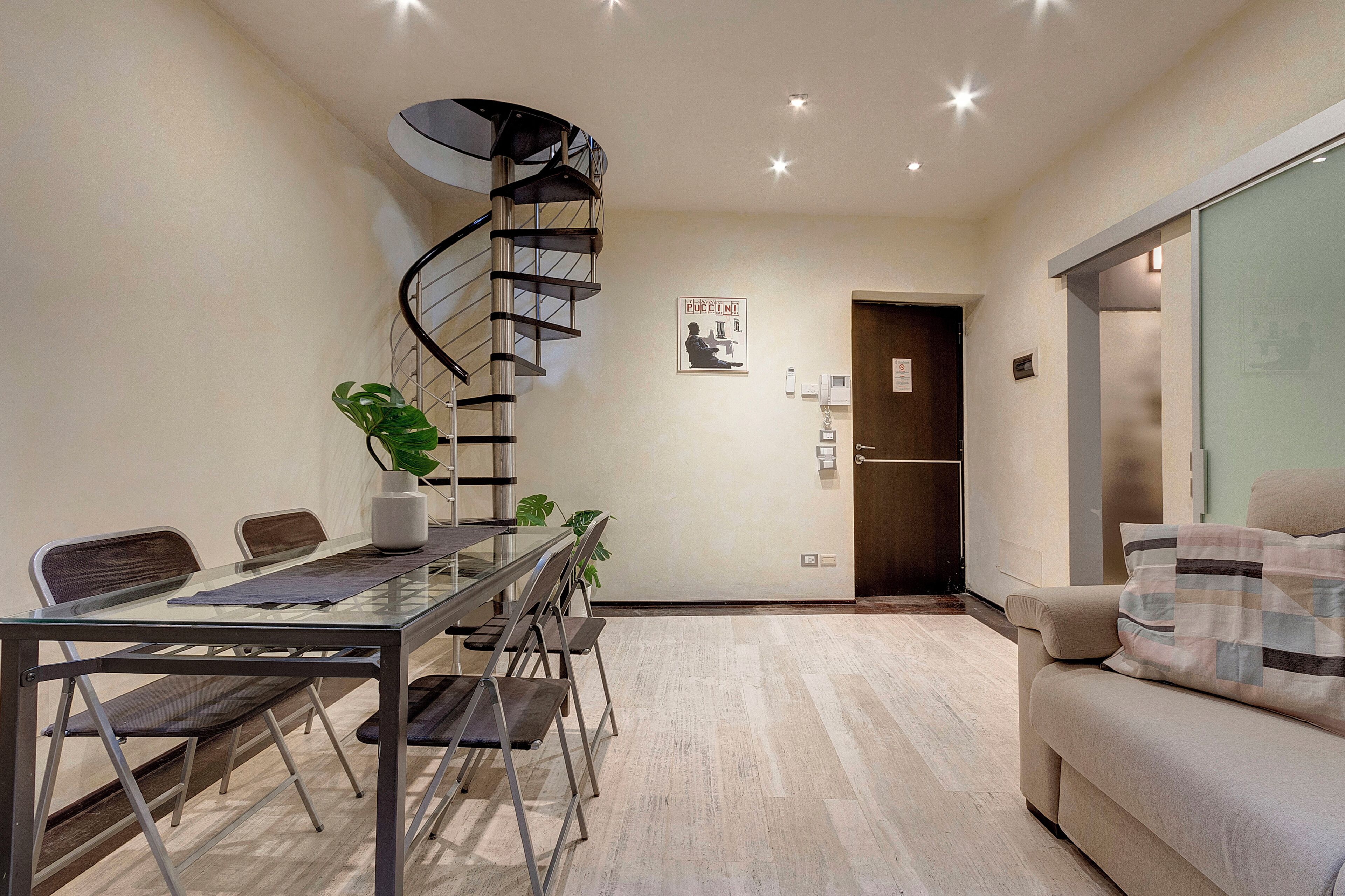 Una sala de estar moderna con una mesa de comedor de vidrio, una escalera en espiral y un sofá.