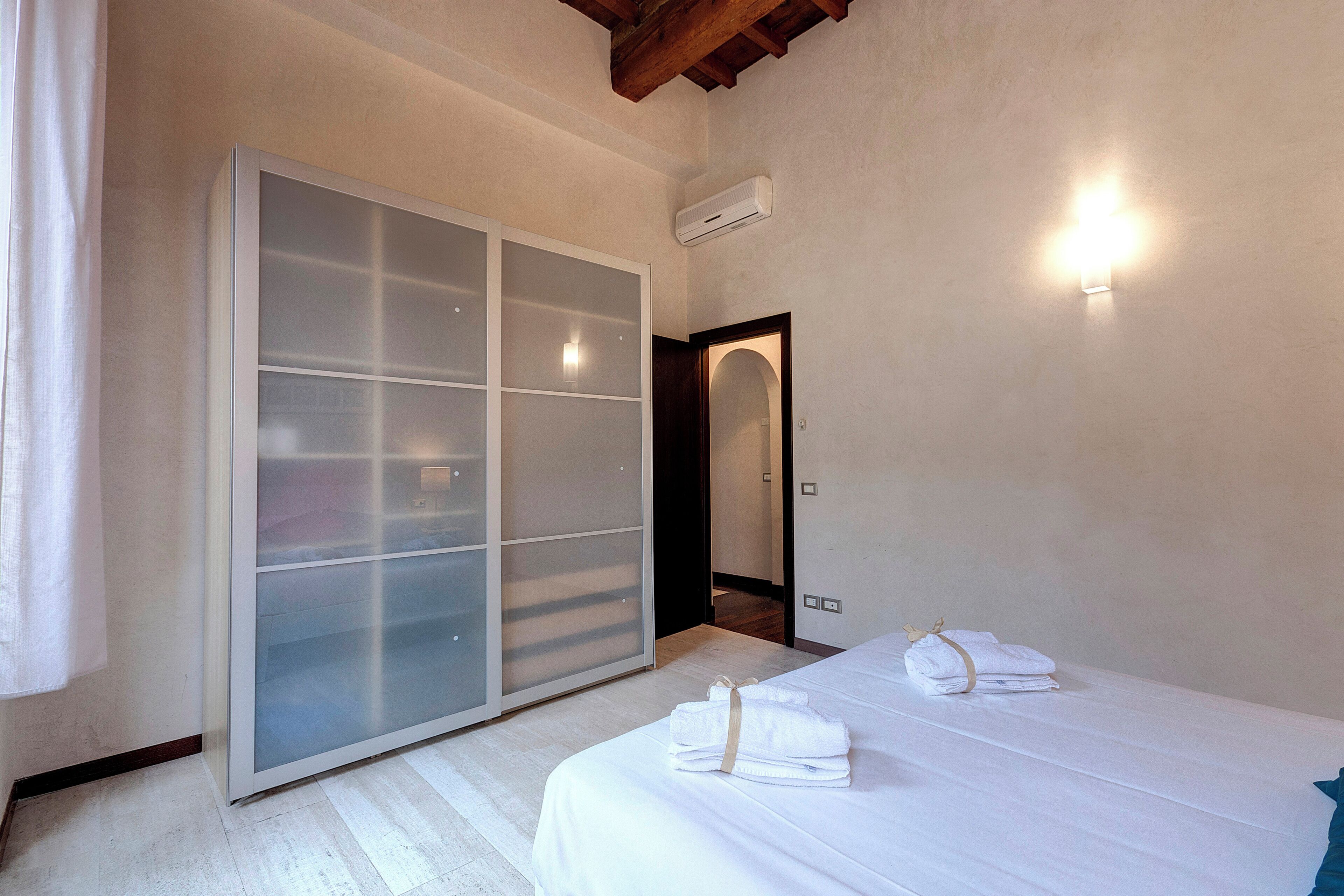Une chambre d’h ôtel dotée d’une grande armoire à portes coulissantes en verre, d’un lit avec des serviettes et d’un climatiseur fixé au mur.