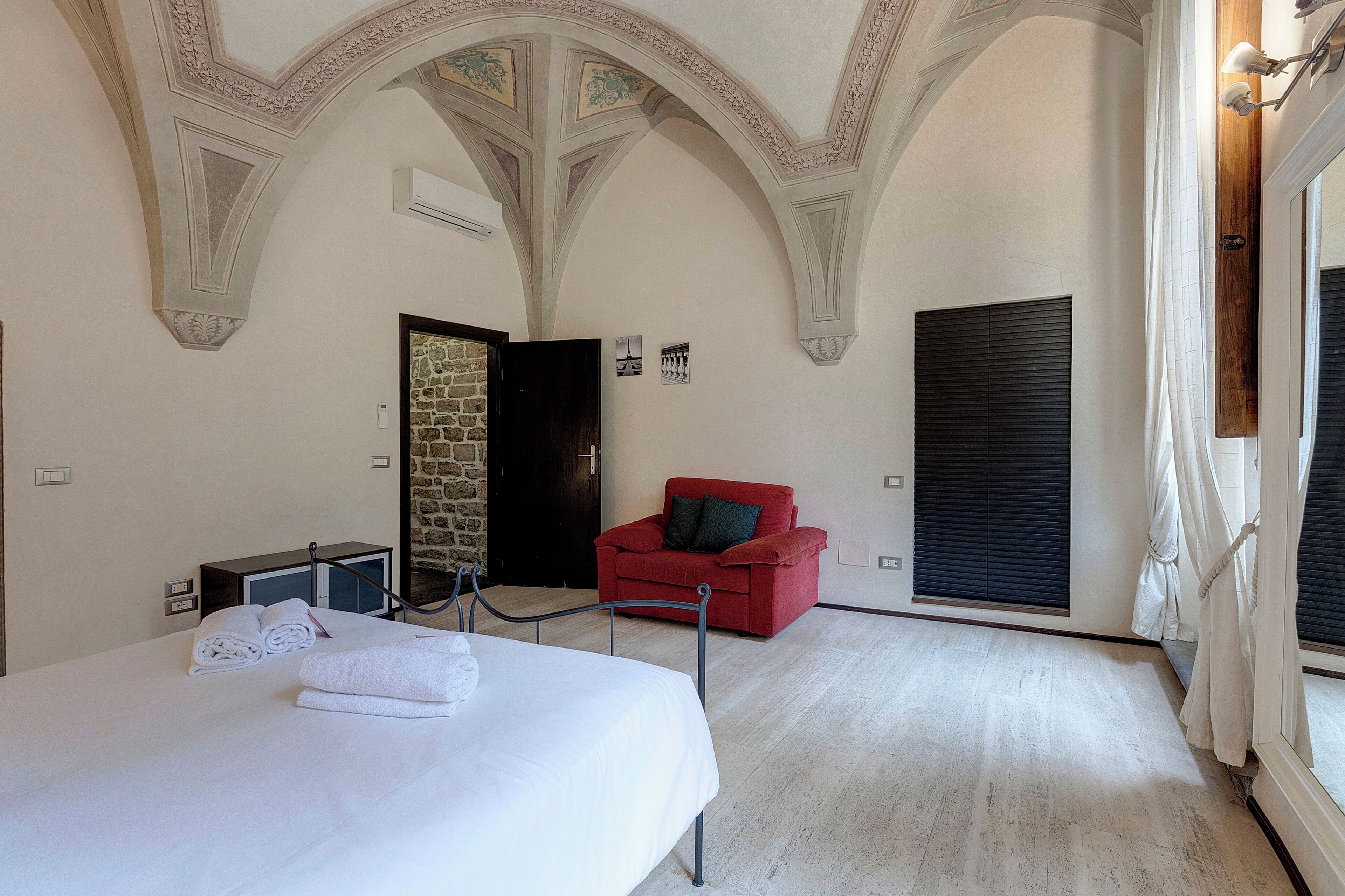 A bedroom with a large bed, a red armchair, and a stone wall.