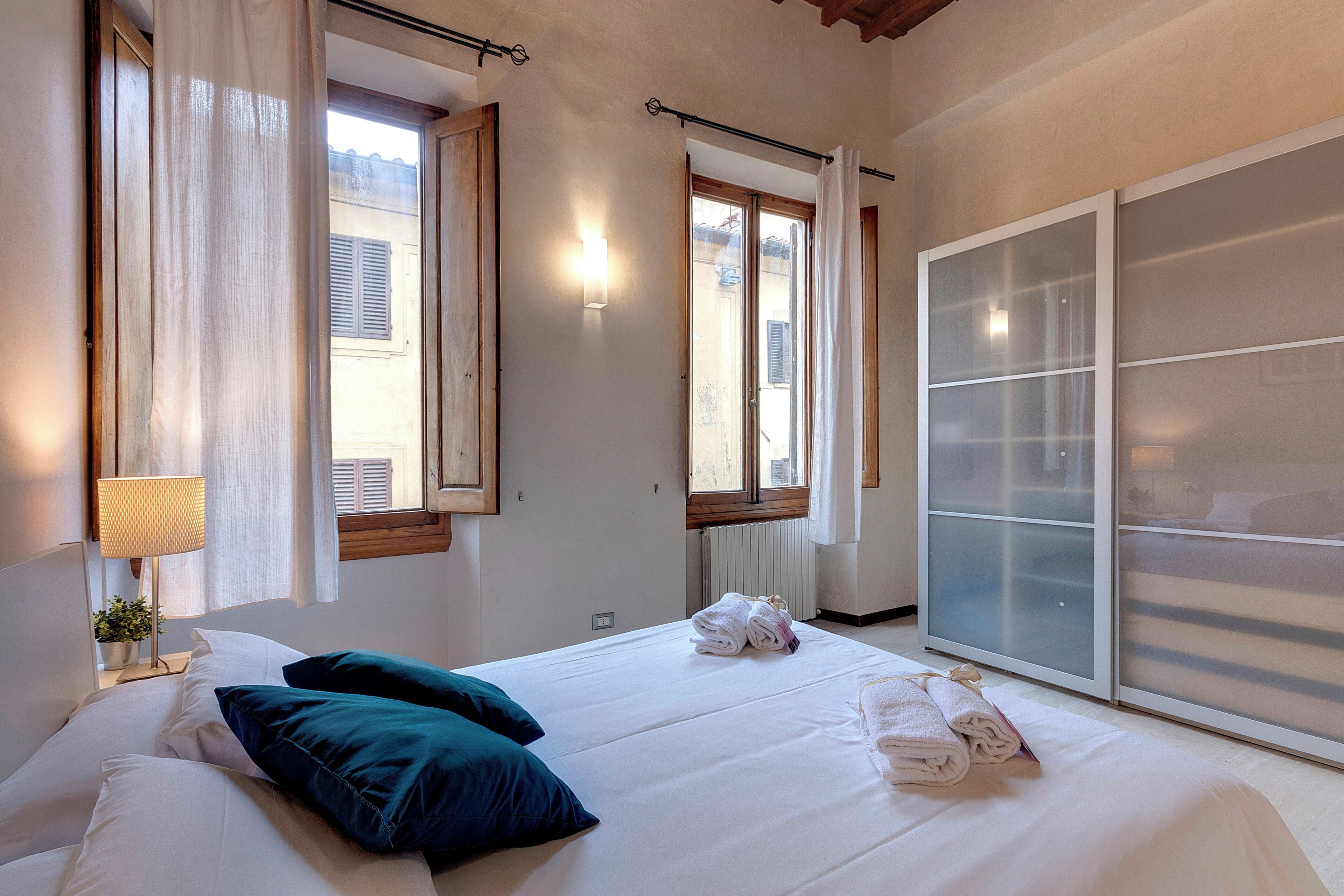 A hotel room with a bed, pillows, a lamp, and a window with curtains.